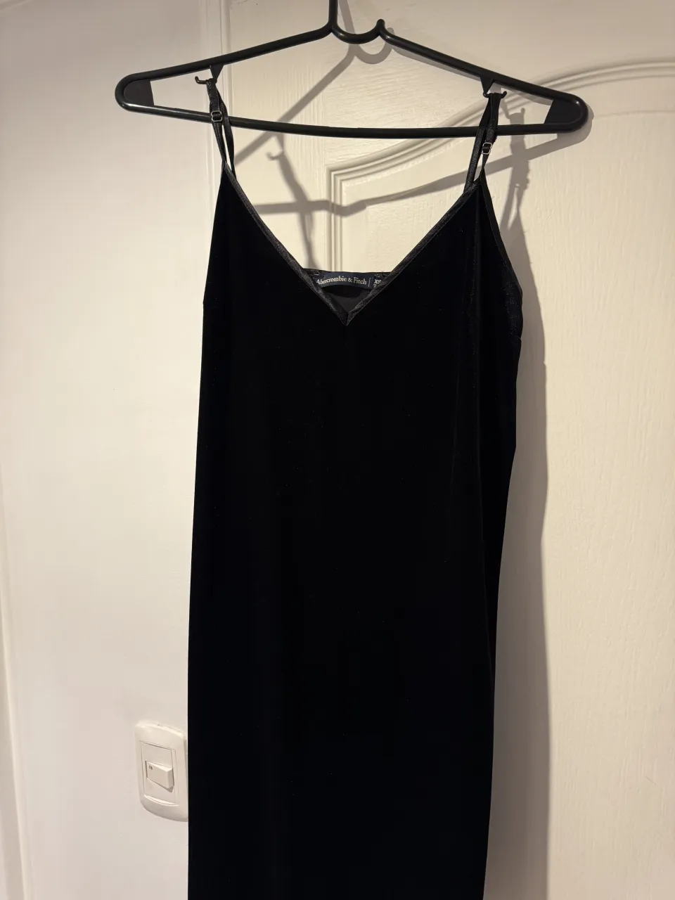 Vestido negro de tirantes finos con escote en V recto, corte arriba de las rodillas.