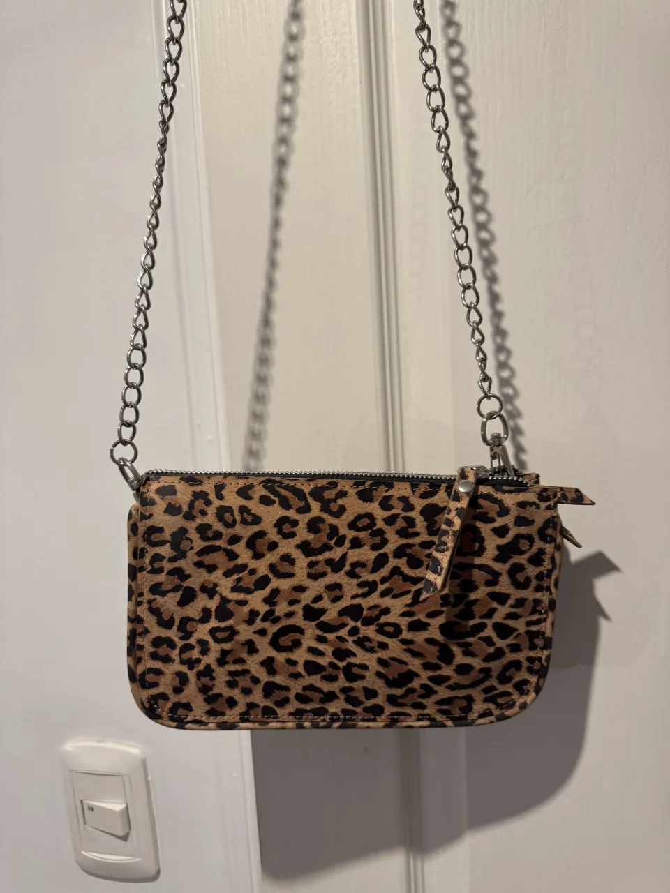 Cartera con estampa de leopardo y cadena metálica. Cierre superior.