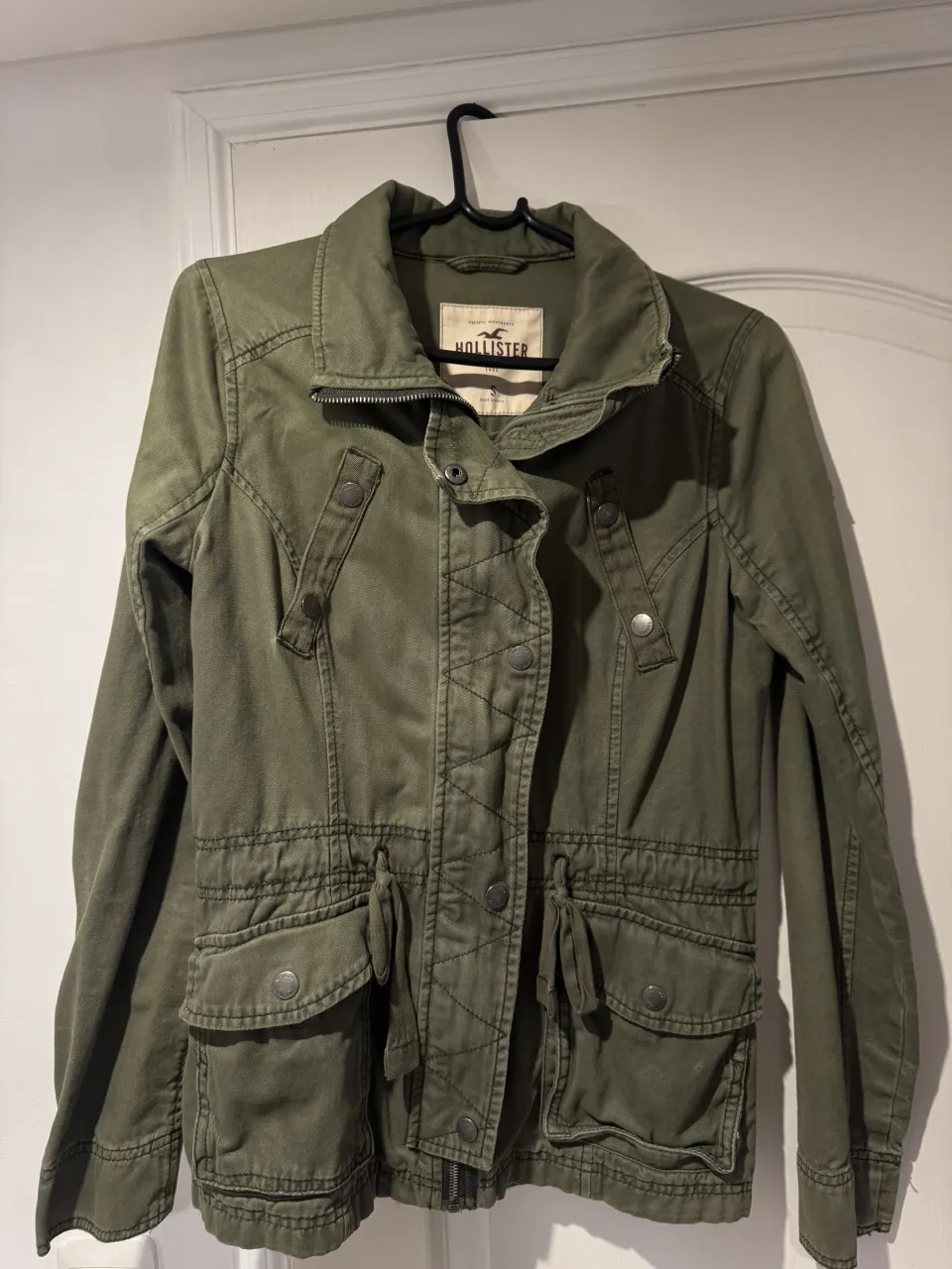 Campera verde con cuello mao, cierre y botones a la vista. Posee bolsillos con solapa en la parte inferior y cordones para ajustar la cintura.