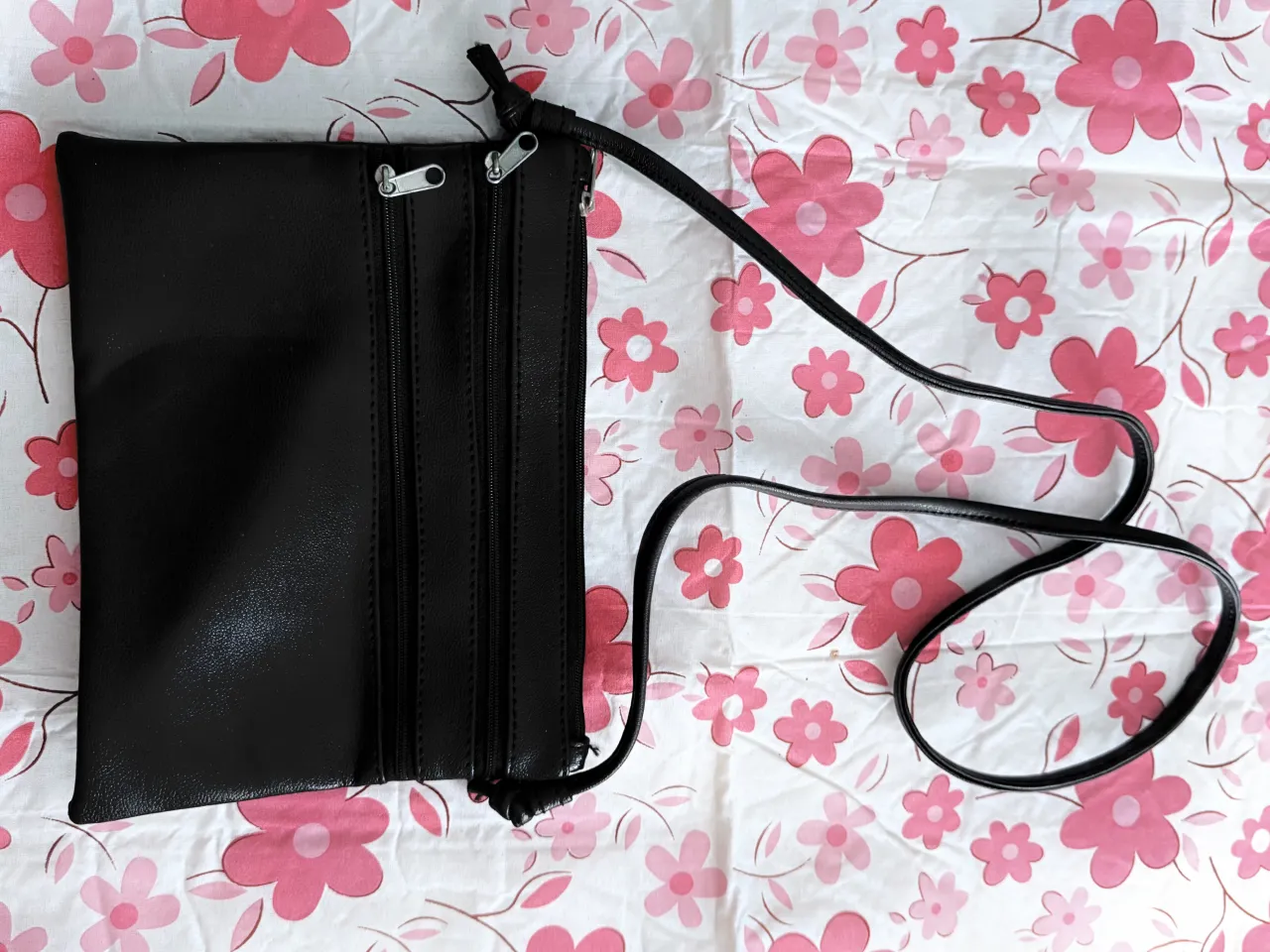 Cartera negra con correa larga y dos cierres frontales. Interior forrado.