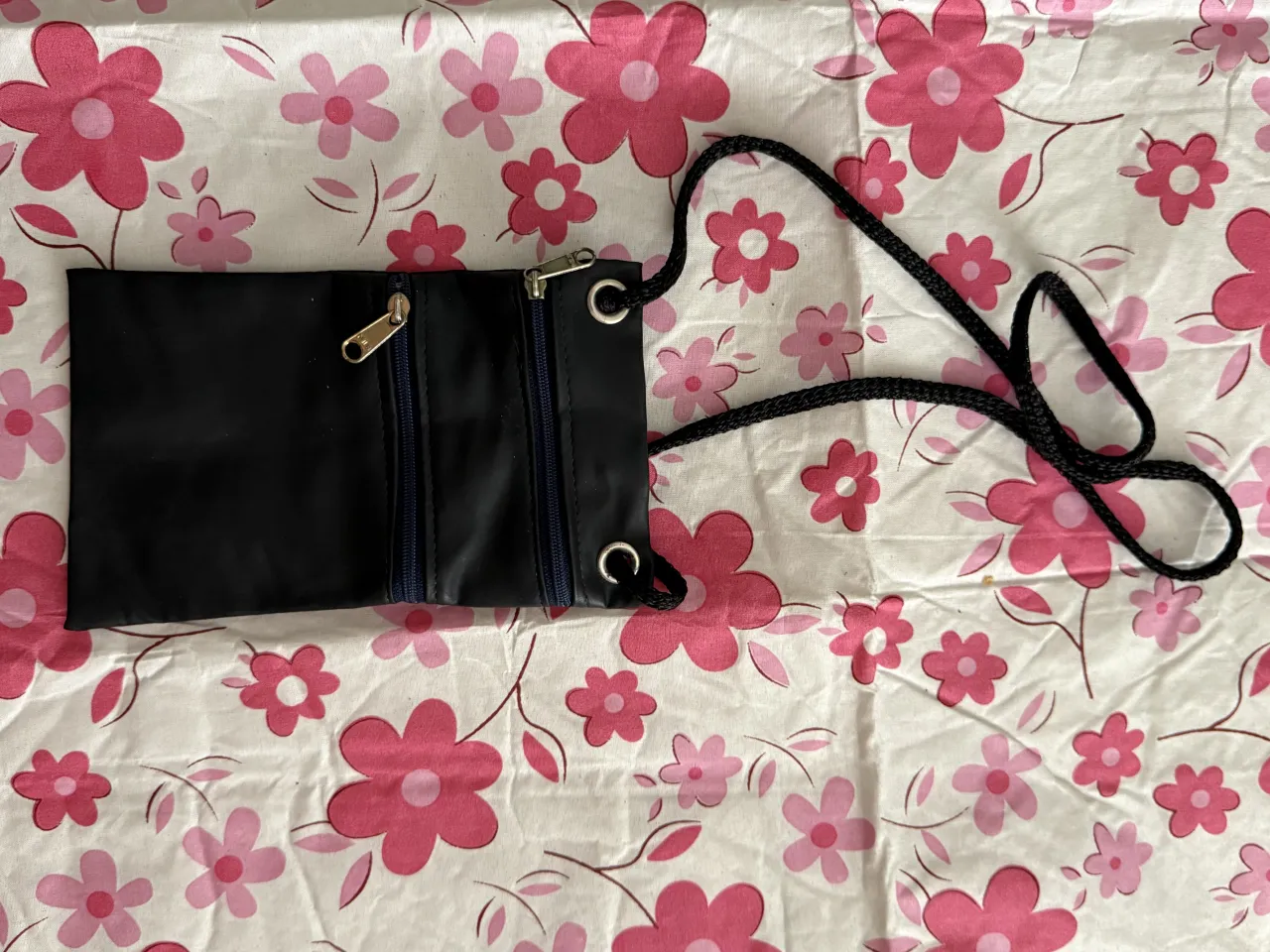 Cartera negra con correa de cuerda negra. Posee dos bolsillos frontales con cierre.