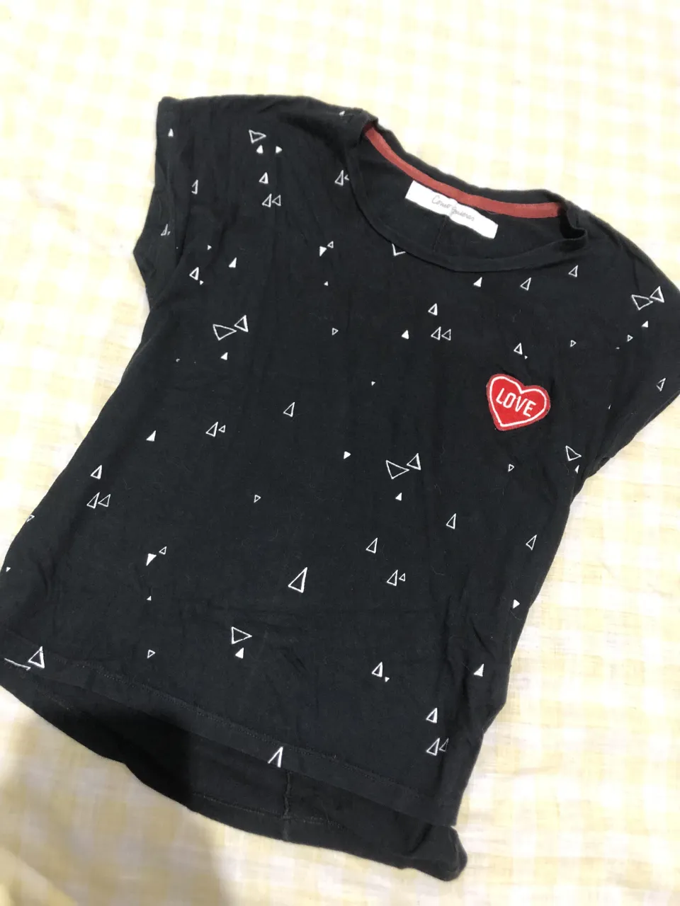Remera negra con estampa de triángulos blancos y un corazón rojo con la palabra "LOVE" bordada. Cuello redondo.