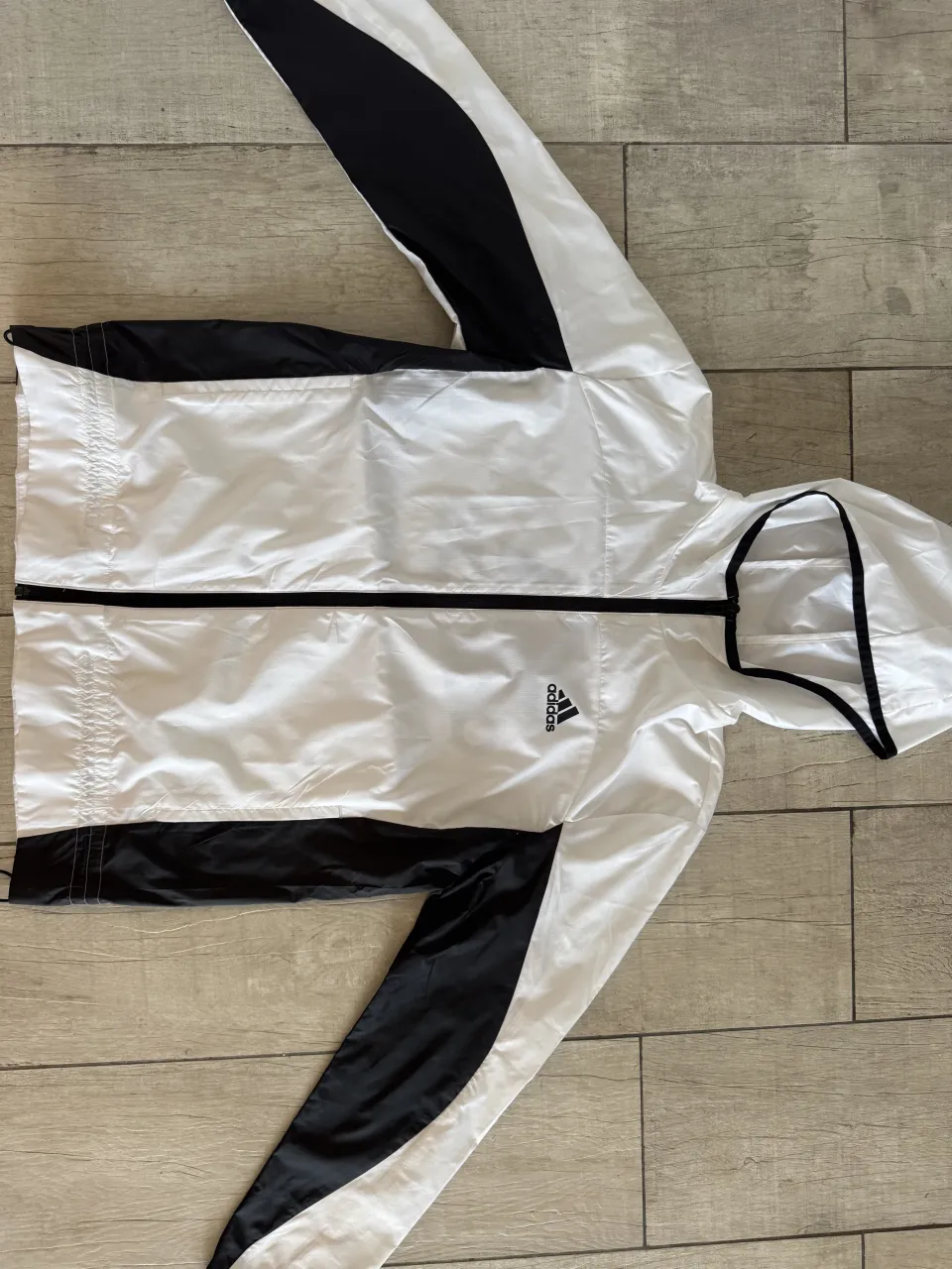 Campera deportiva blanca con detalles en negro en mangas y laterales. Capucha con cordón y logo de Adidas estampado en el frente y la espalda.