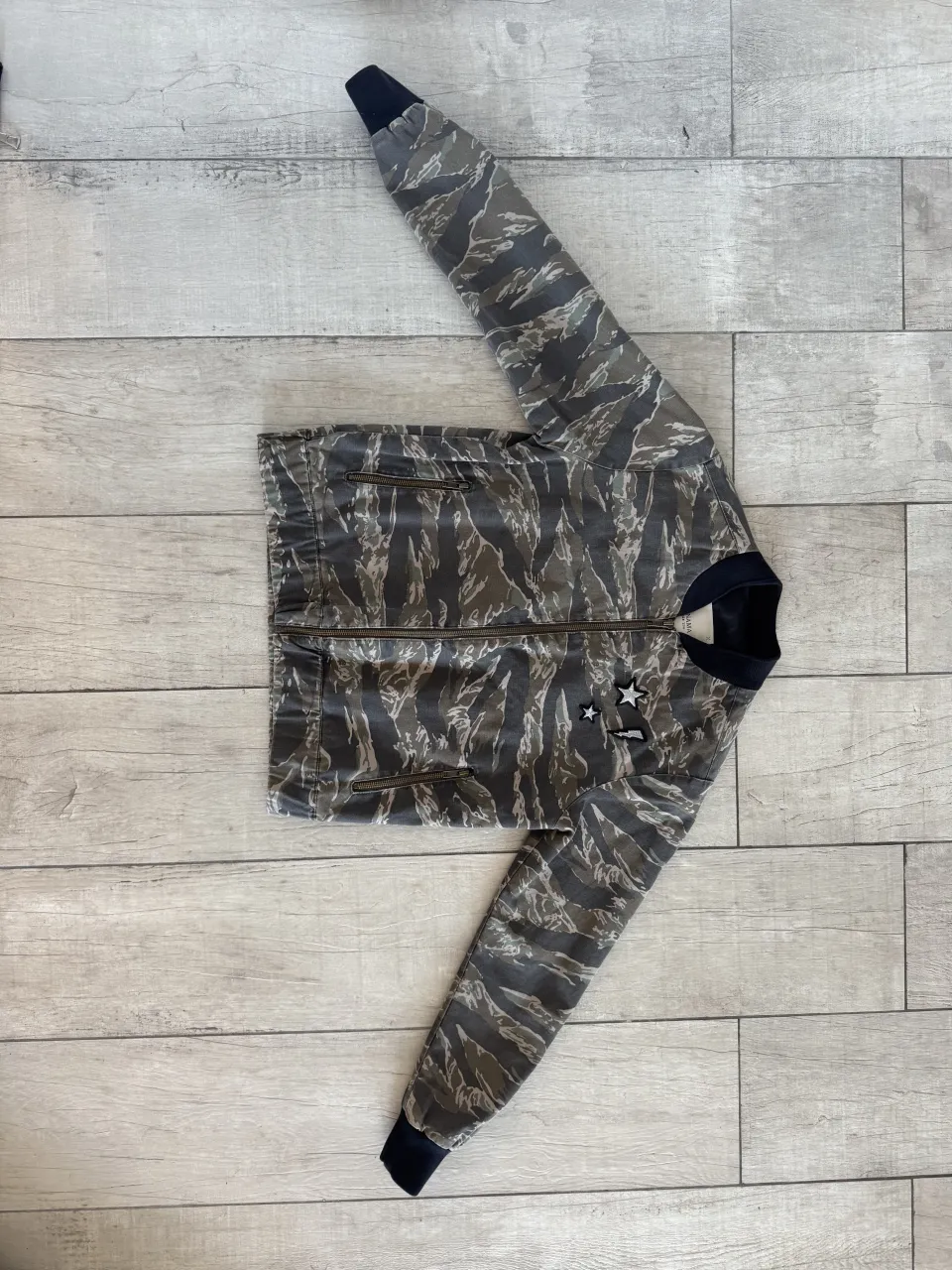 Campera bomber con estampa camuflada y dos estrellas blancas bordadas en el frente. Cierre metálico y puños elastizados.