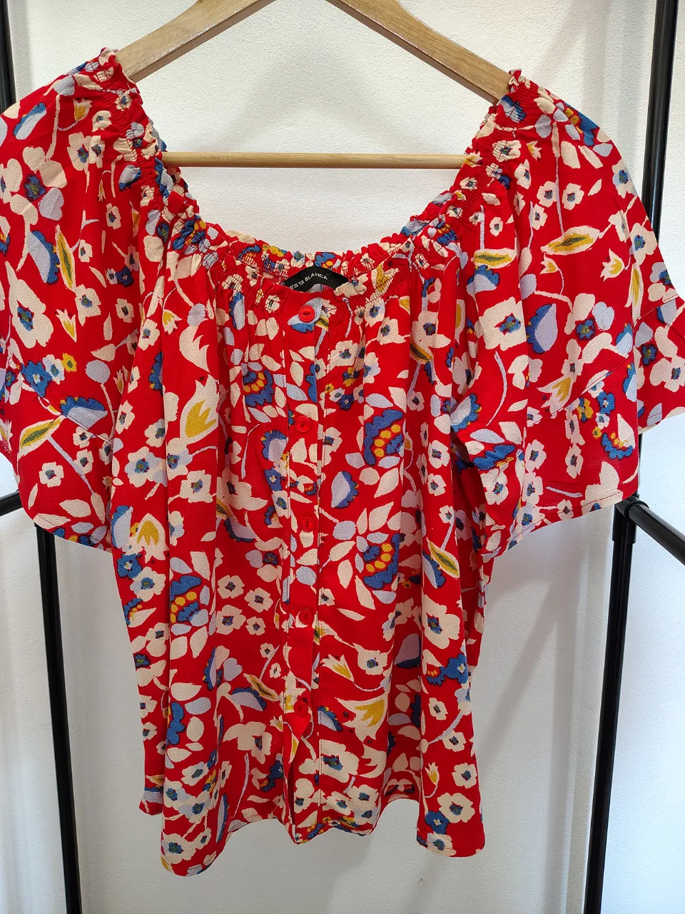 Blusa en bambula roja con estampado floral multicolor. Posee cuello con elástico y mangas cortas. Tiene botones al frente.