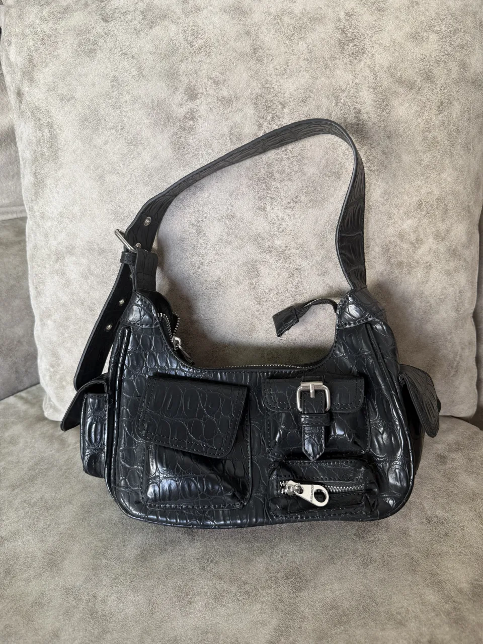 Shoulder bag negra con textura de cocodrilo. Posee múltiples bolsillos y cierre metálico.