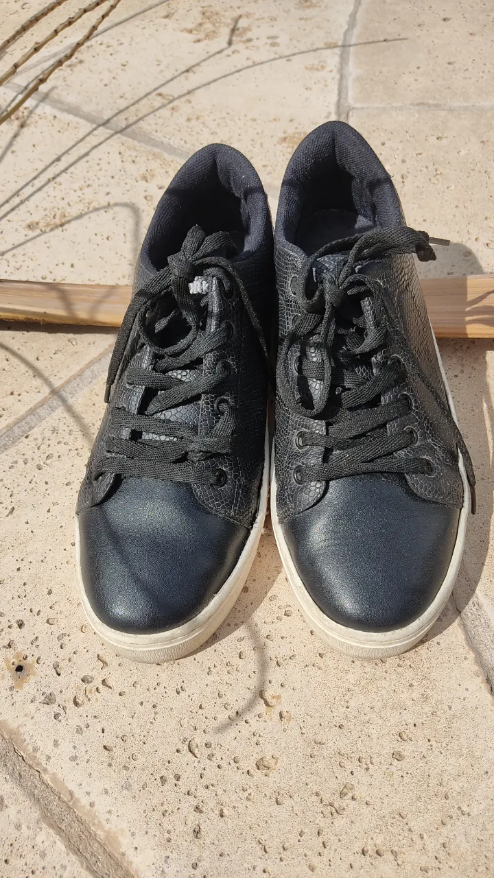 Zapatillas urbanas de cuero vegano negro, partes laterales con texturas tipo animal print, cordones del mismo color. Suela plana de goma color natural, mide 2,5cm. 
La plantilla mide 25,5cm