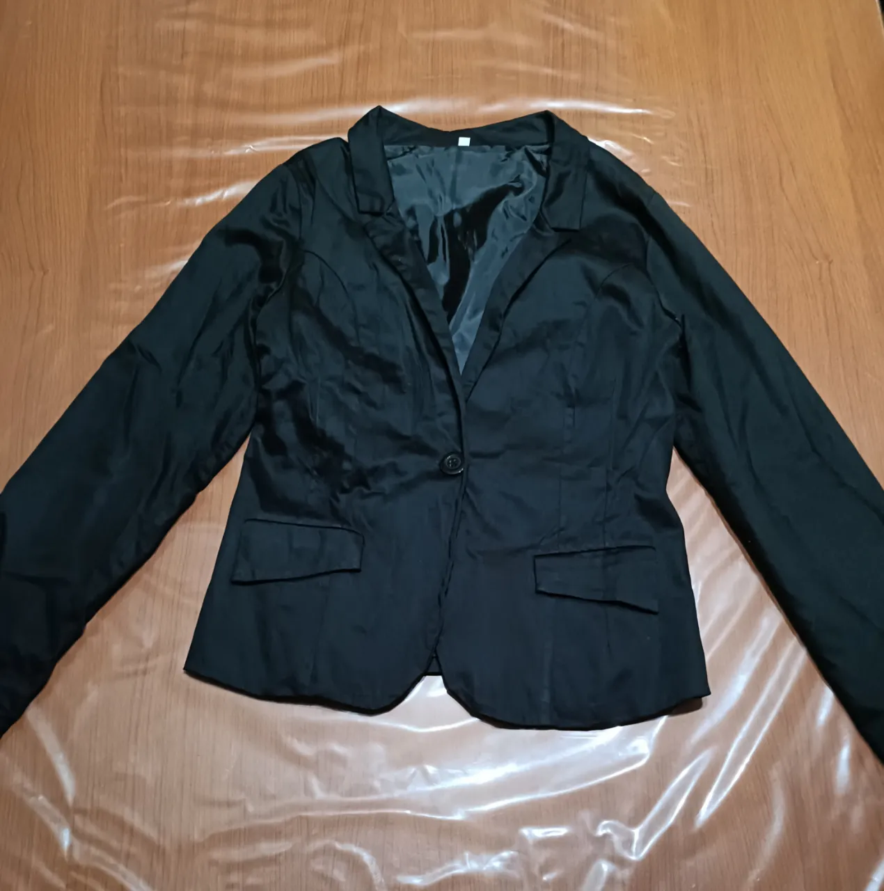 Blazer negro de vestir con un botón al frente al tono y dos bolsillos con solapa. Posee forro interior y la tela elastiza un poco.