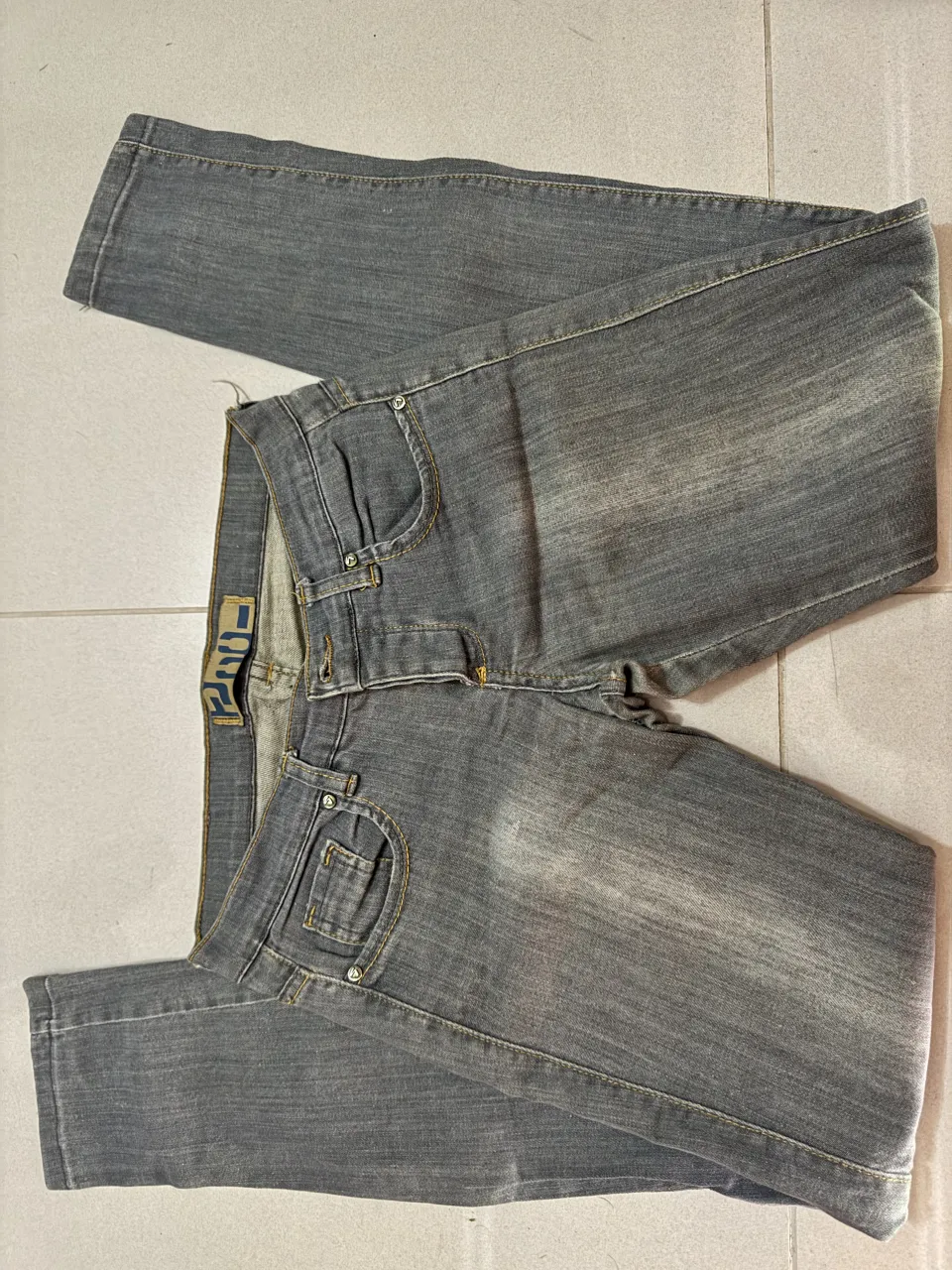 Jeans grises con costuras amarillas. Presentan bolsillos delanteros y traseros.