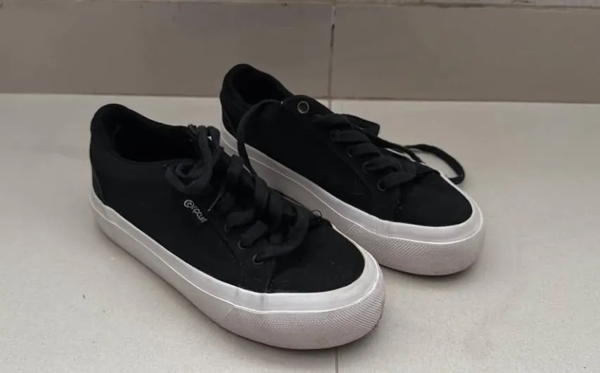 Zapatillas negras con cordones y suela blanca.