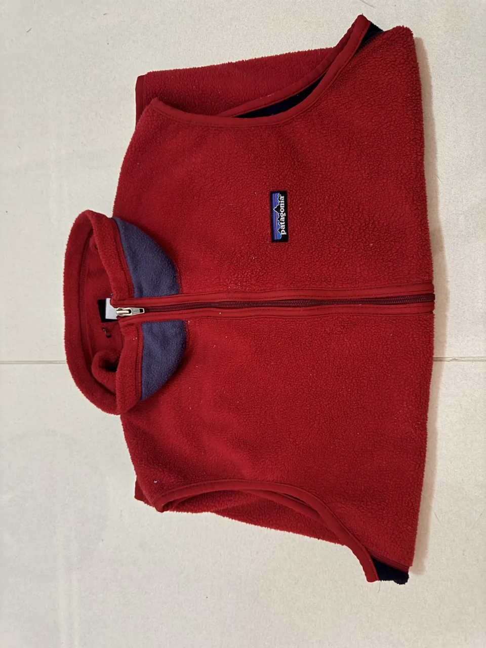 Chaleco de polar rojo con cuello y detalles en azul marino. Posee cierre frontal y un bolsillo con cierre en la espalda.