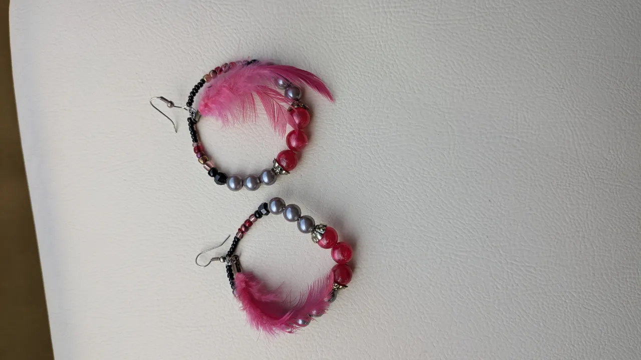 Aros colgantes con cuentas rosas, grises y negras, y plumas rosas.