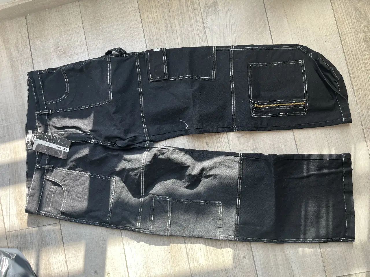 Pantalón cargo negro con detalles en blanco y cierre en el bolsillo. Talle 38, estilo utilitario y streetwear.
