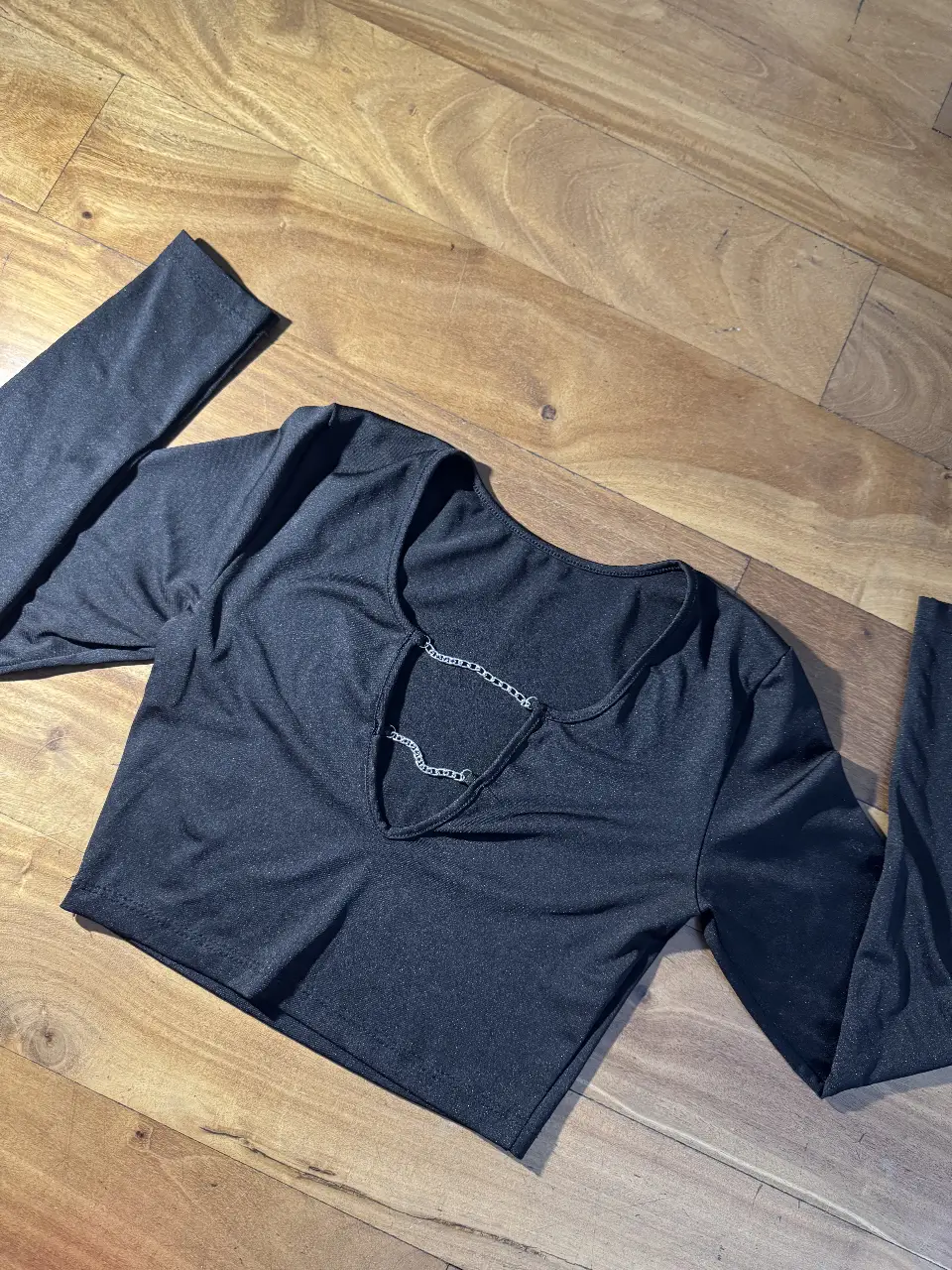 Top negro de manga larga con escote en V y detalle de cadena. Ideal para un look moderno y sofisticado.