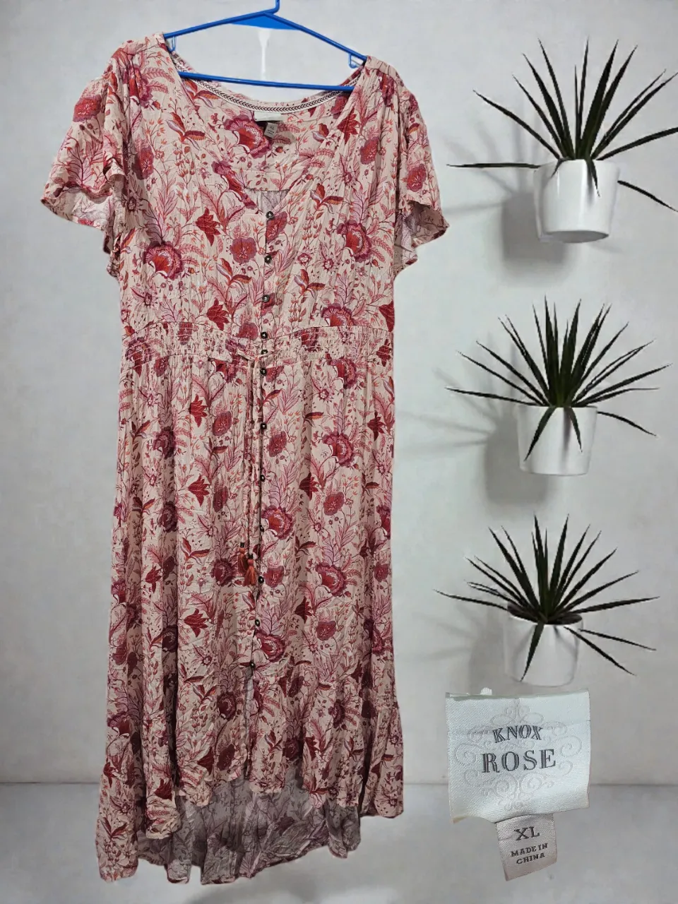 Vestido largo estampado floral en tonos rosas y rojos. Posee cuello en V, botones al frente y mangas cortas con volados. La cintura es elastizada y la falda tiene un corte irregular con volados sutiles. Ideal para un look casual y femenino.
