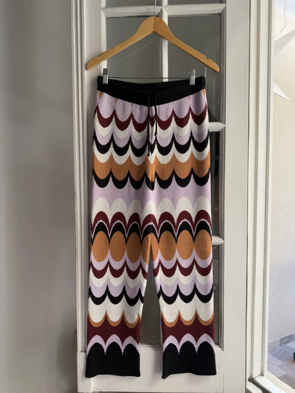 Pantalón tejido con estampado de ondas y círculos en colores lila, blanco, bordó, naranja, negro y marrón. Cintura elastizada con cordón.