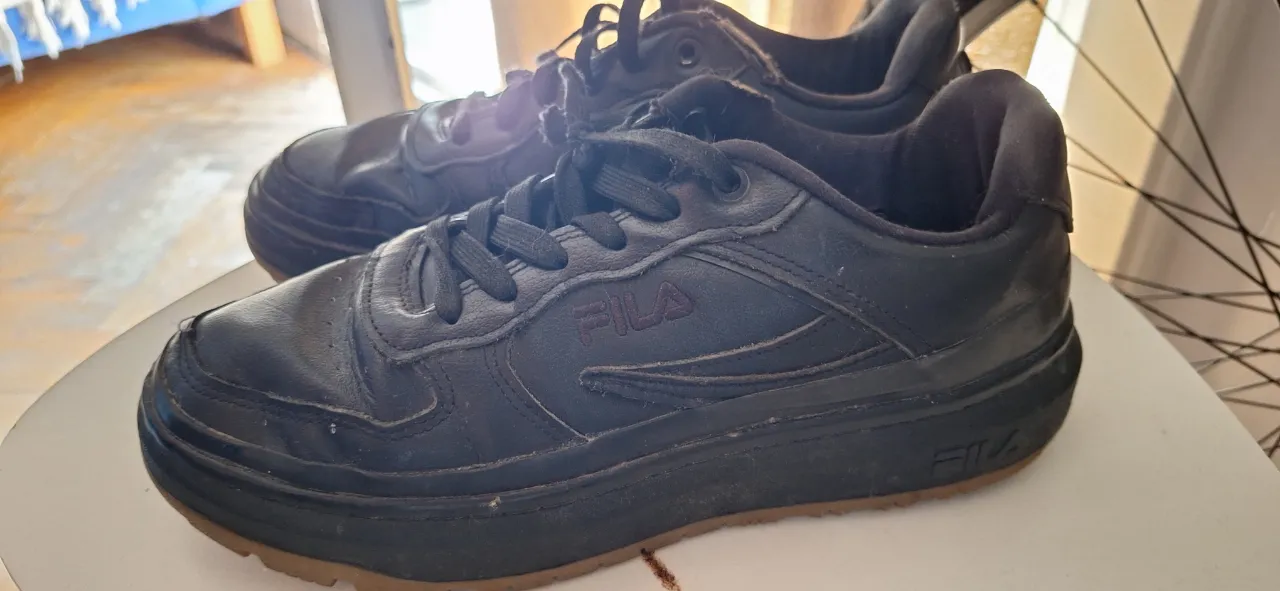 Zapatillas urbanas negras de cuero sintético, sin cordones. Tienen suela gruesa y el logo de la marca en los laterales y en la lengüeta.