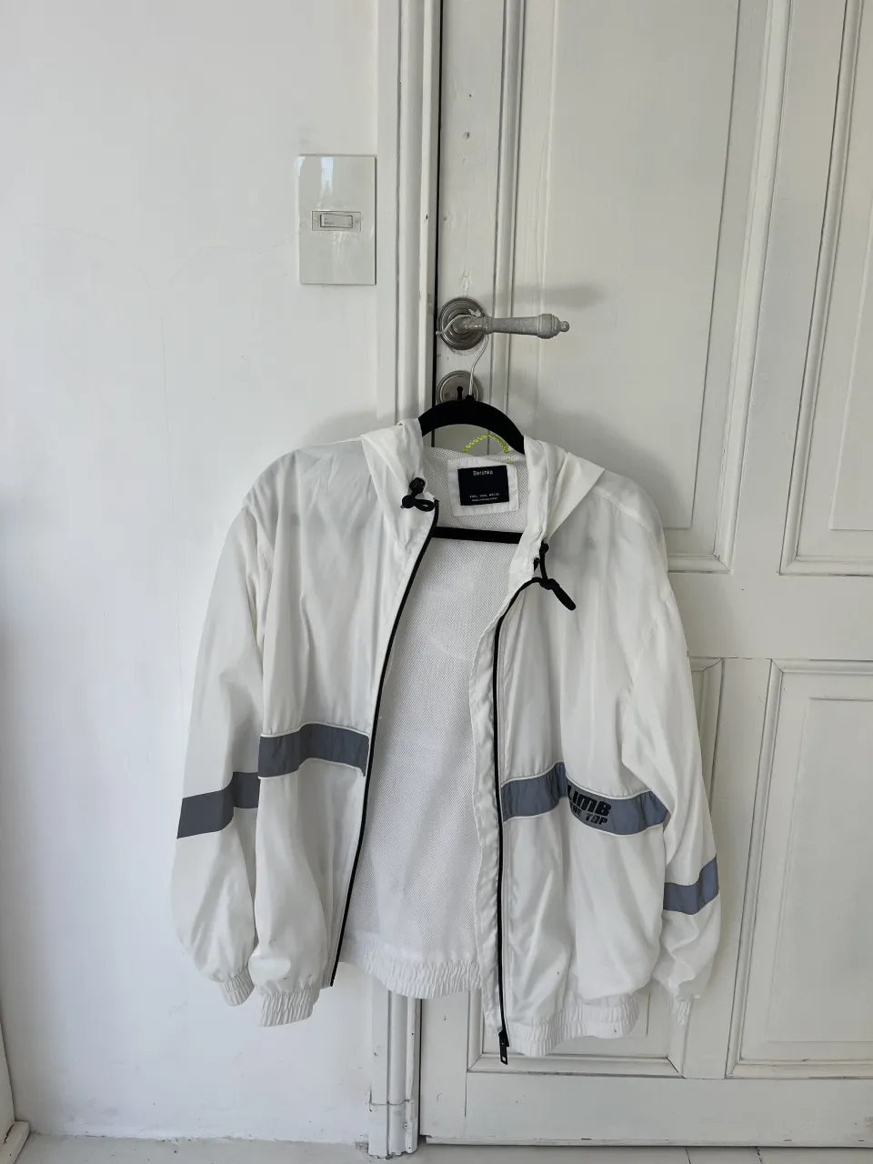 Campera blanca con capucha y cierre. Posee detalles reflectantes en mangas y espalda. Logo de la marca en el frente.