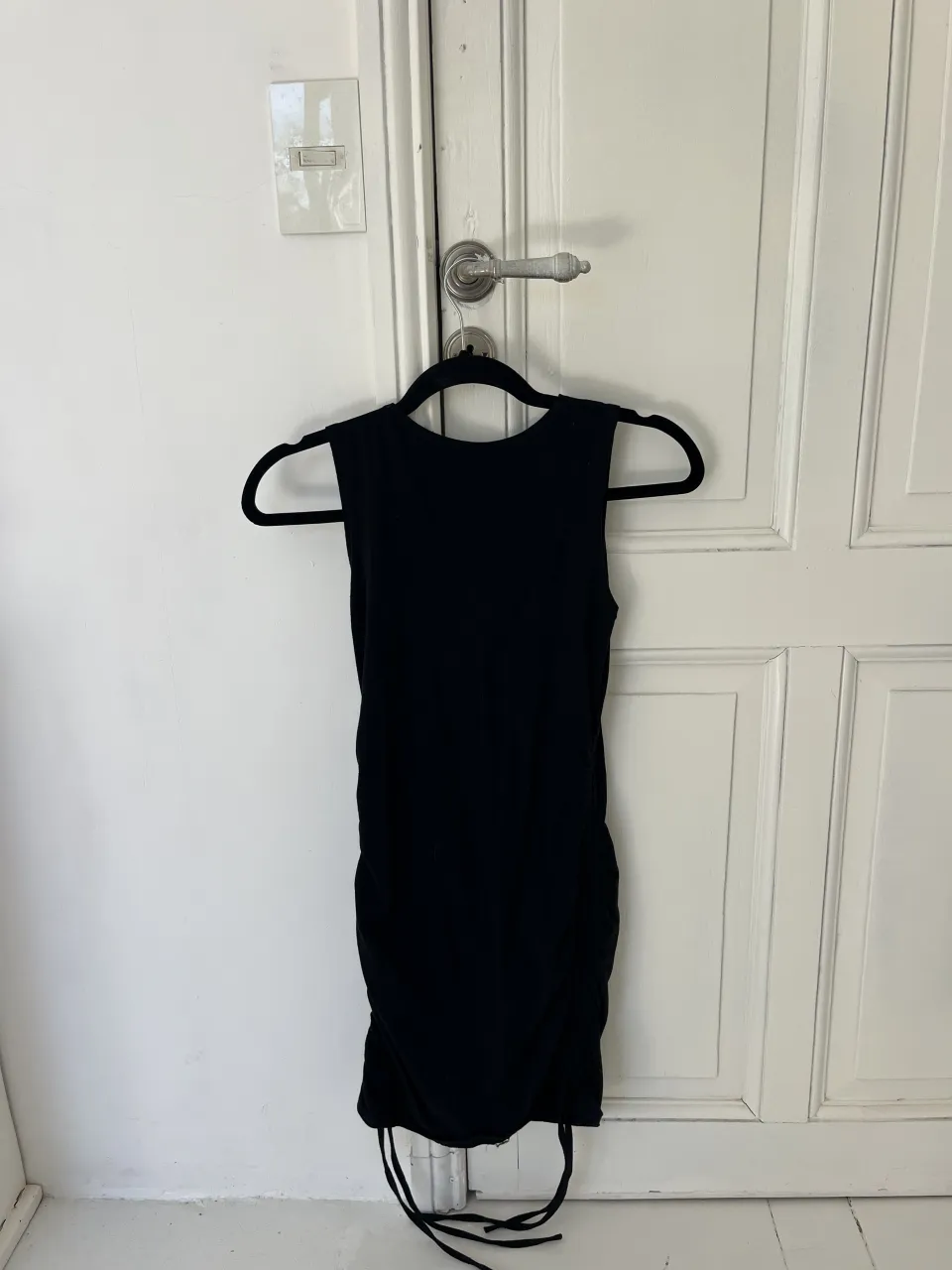 Vestido negro sin mangas con fruncido lateral y cordones ajustables en el bajo.