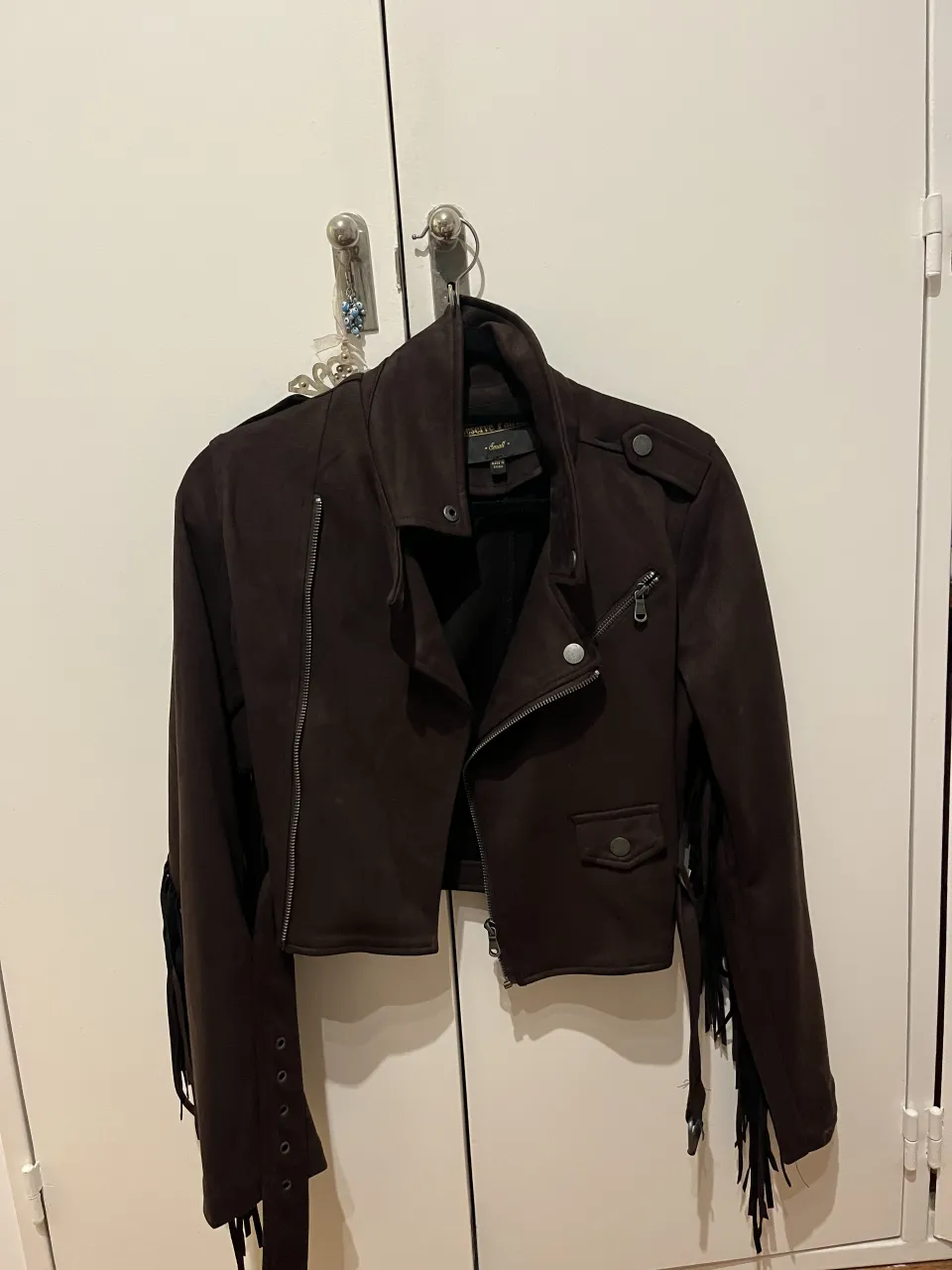 Campera corta de gamuza marrón con flecos largos en mangas y espalda. Cierre metálico al frente y bolsillos con broches.