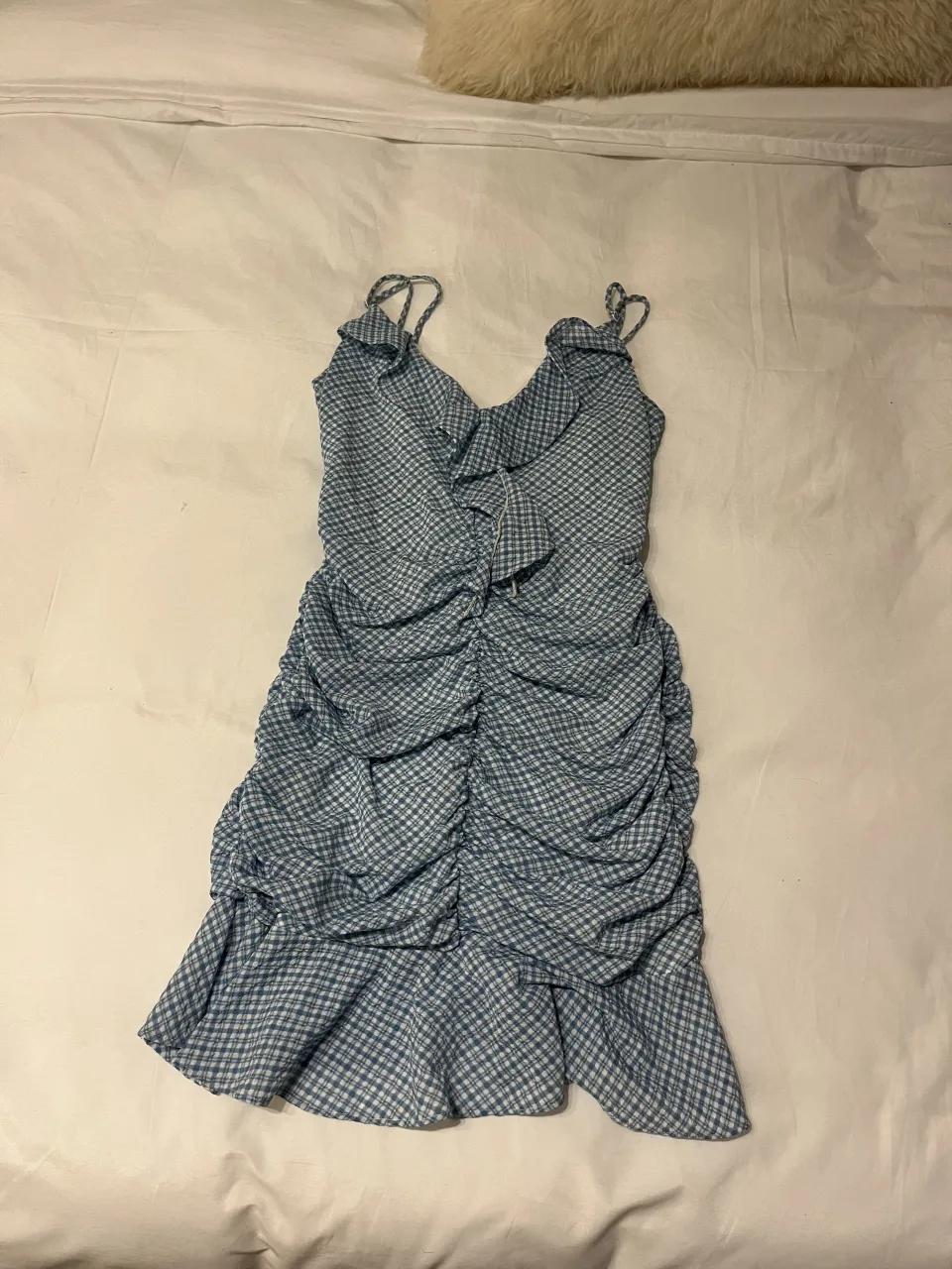 Vestido corto con estampado a cuadros pequeños en tonos azules y blancos. Posee volados en el escote y fruncido en toda la parte delantera y trasera de la falda. Breteles finos.