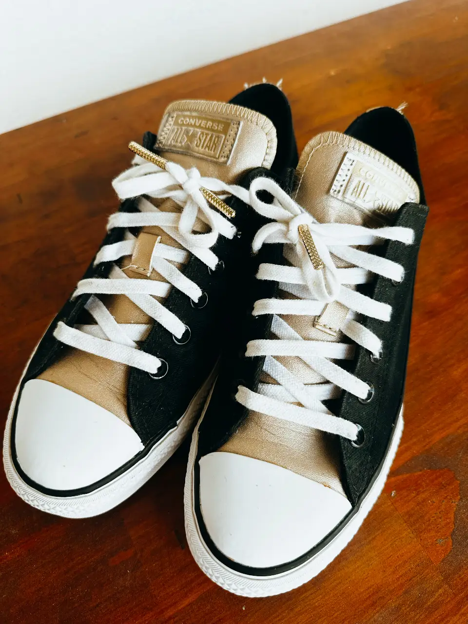 Zapatillas Converse All Star de lona en color negro y detalles dorados. Diseño clásico con puntera blanca y cordones blancos. Ideales para un look casual y urbano.