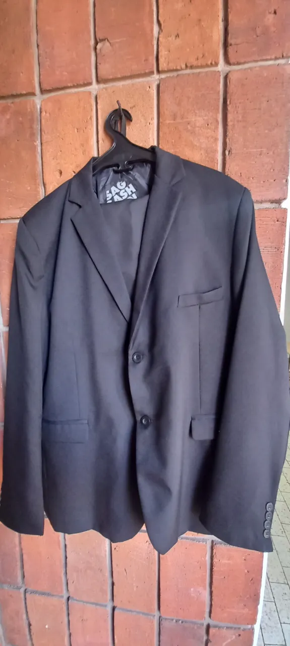 Traje de saco y pantalón negro. El saco tiene dos botones al frente y bolsillos con solapa. El pantalón es liso.