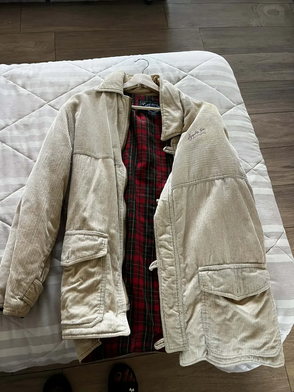 Campera de pana color crudo con forro a cuadros escoceses en rojo y negro. Posee dos bolsillos con solapa en la parte delantera. Es super abrigada