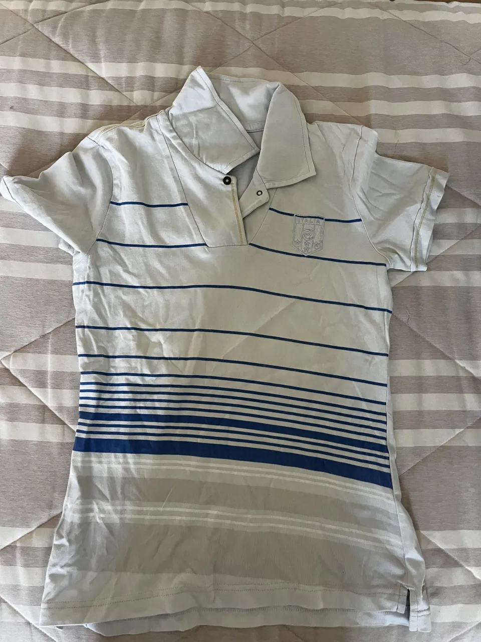 Chomba puma a rayas horizontales azules y grises. Tiene un escudo bordado en el frente izquierdo con la inscripción "ITALIA".