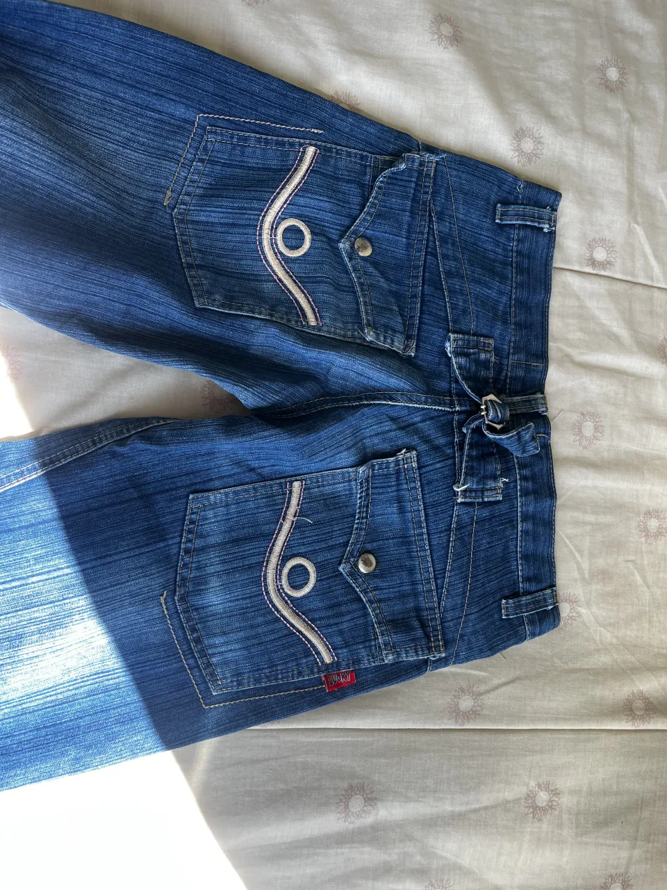 Jeans de tiro bajo con bolsillos delanteros y traseros con tapa y botón. Detalle de pespuntes blancos y bordes en los bolsillos.