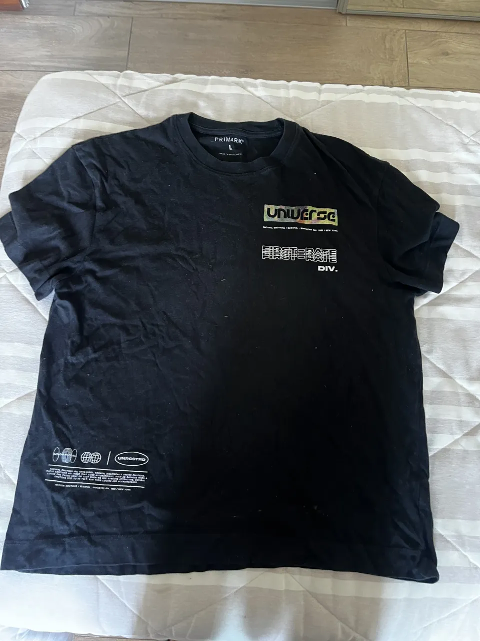 Remera negra de manga corta con estampa gráfica en frente y espalda. La estampa del frente tiene el logo "UNIVERSE" y "FIRST-RATE". La estampa de la espalda tiene un diseño más grande con la palabra "BLISSFUL" y un insecto.