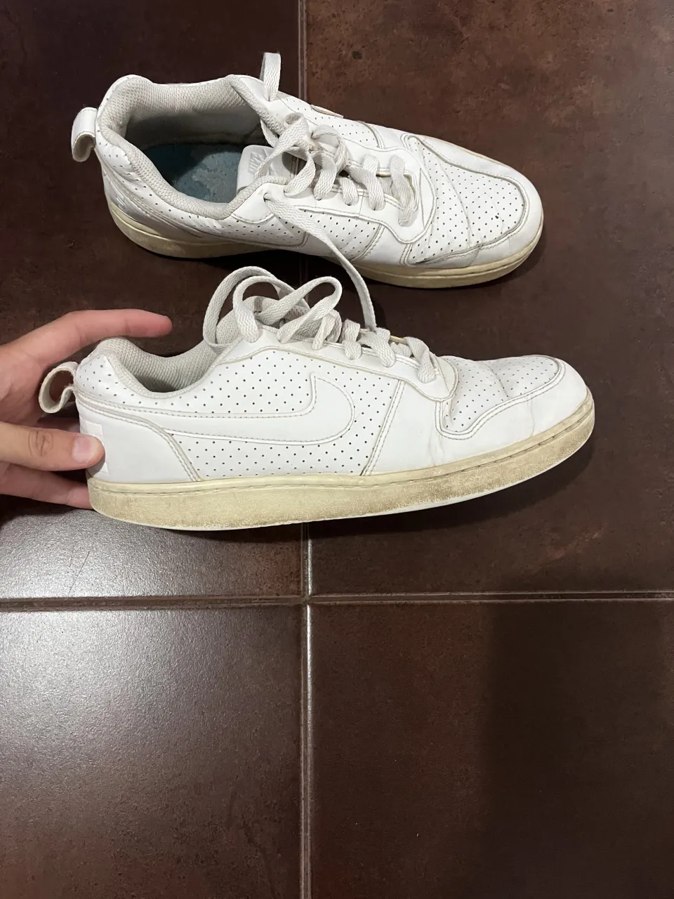 Zapatillas Nike blancas de cuero con cordones y detalles perforados. Tienen el logo de la marca en los laterales y en la lengüeta. Le faltan las plantillas