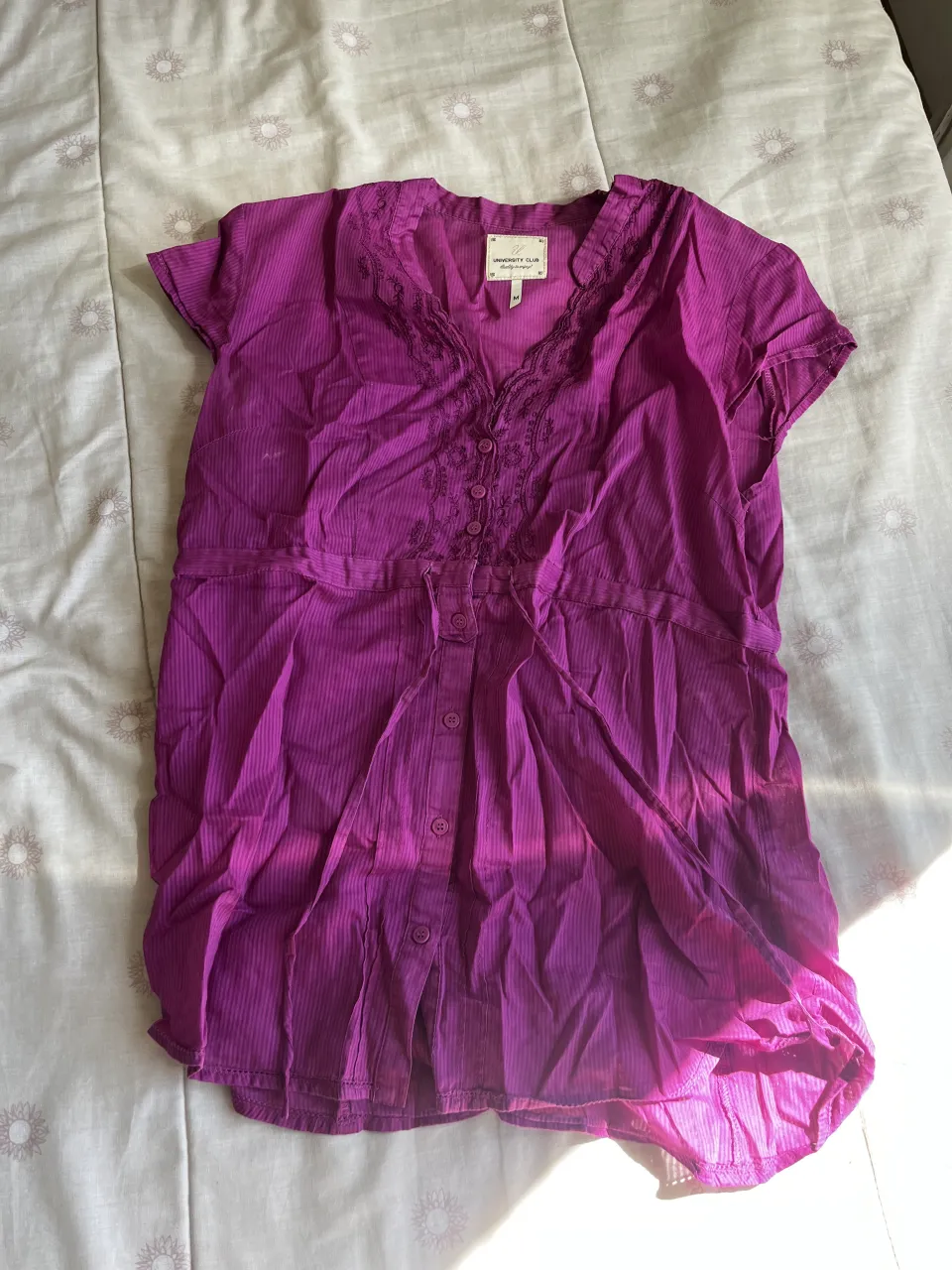 Camisa manga corta de color fucsia con detalles de bordado y encaje en el cuello. Posee botones en la parte delantera.