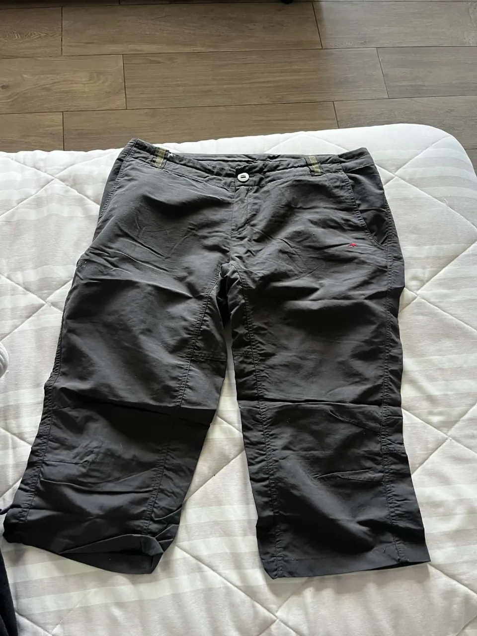 Pantalón capri de color gris oscuro, con bolsillos delanteros y traseros. Posee un pequeño detalle bordado en color rojo en el bolsillo delantero derecho.  El largo de la pierna es hasta la rodilla.