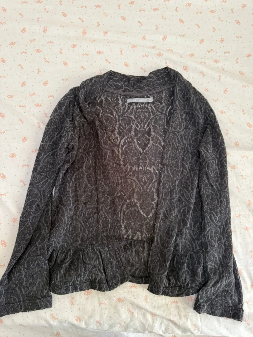 Cardigan gris con estampado floral en relieve y volado en la parte inferior.