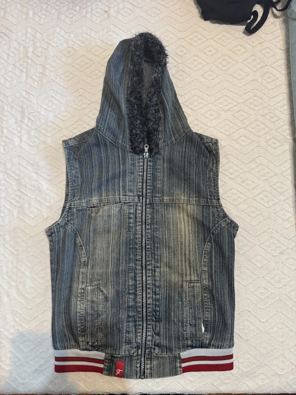 Chaleco de jean con capucha forrada en peluche. Cierre completo al frente. Puños con franjas rojas y blancas.