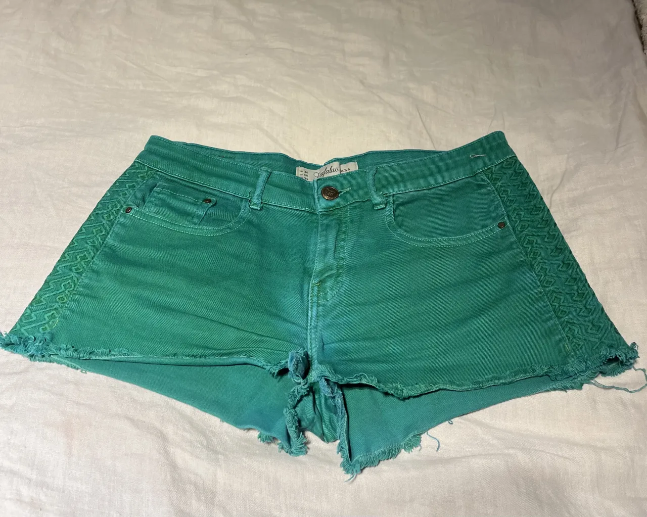 Shorts de jean color verde con detalles de bordado en los laterales y terminación desflecada en el bajo.