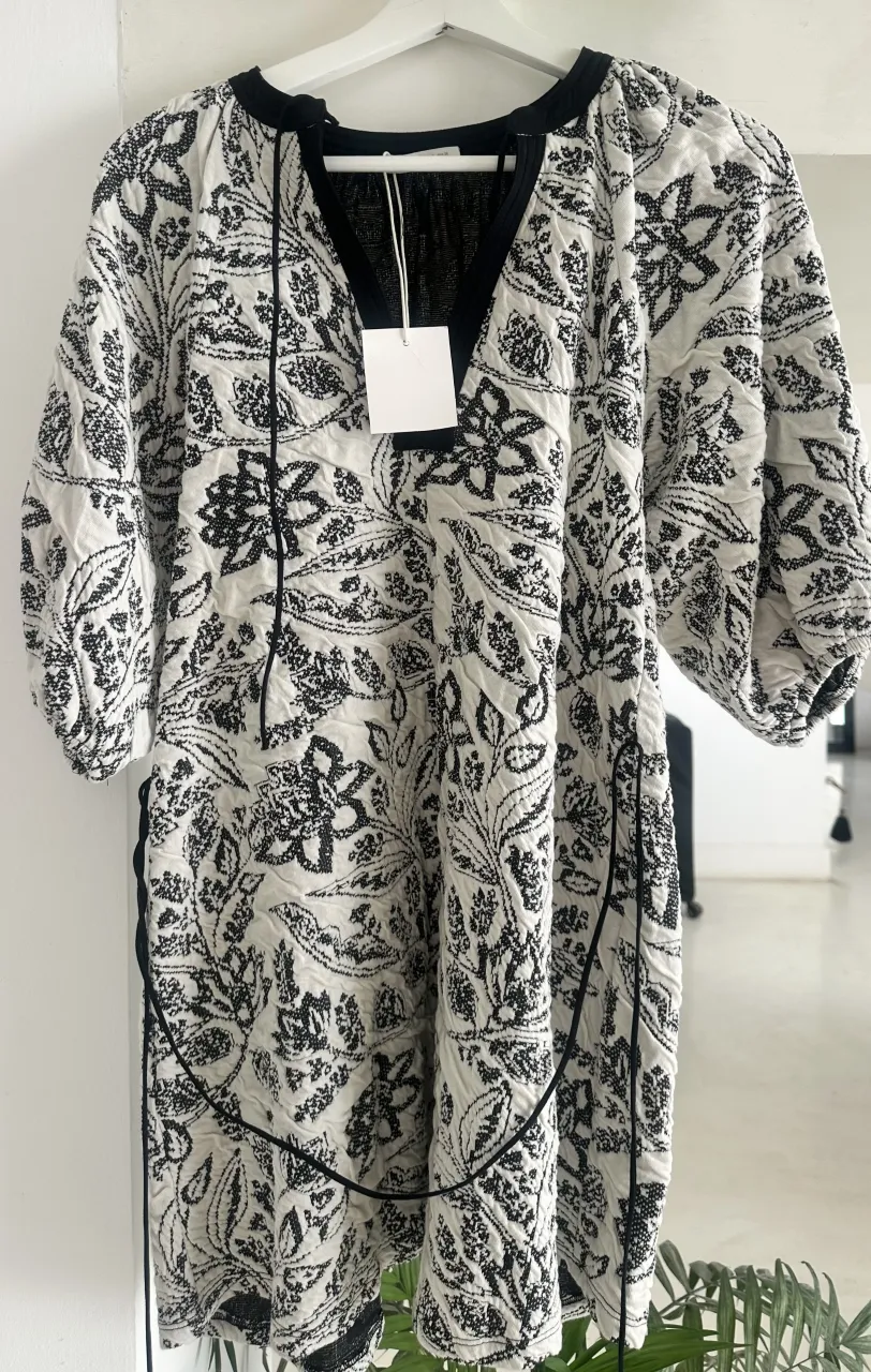 Blusa blanca con estampa floral en negro. Posee cuello en V con cordones para atar. Mangas largas abullonadas con puño.