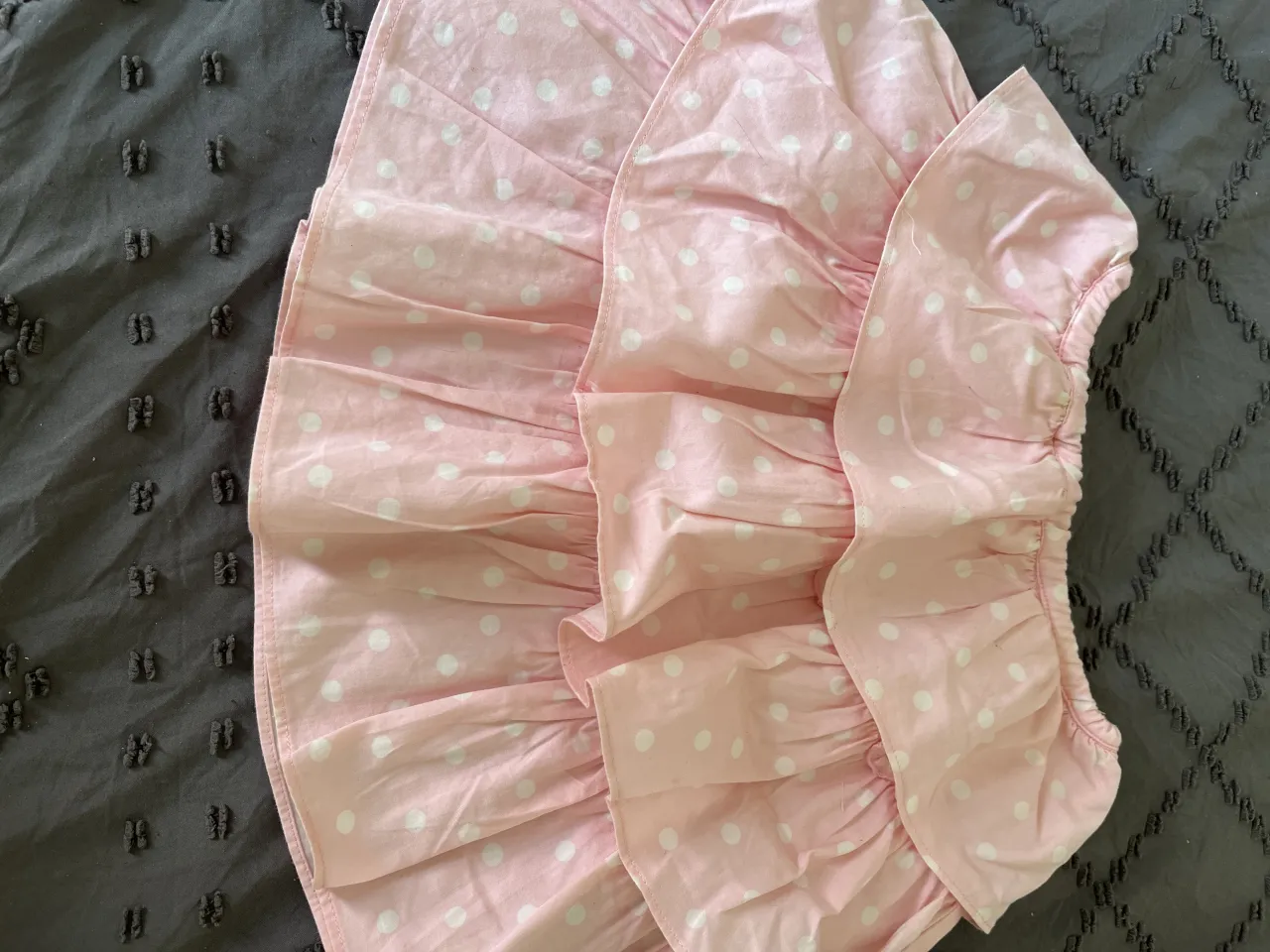 Vestido rosa con lunares blancos, ideal para niñas. Tiene volados y un detalle de botones en la parte superior. Perfecto para un look tierno y divertido.