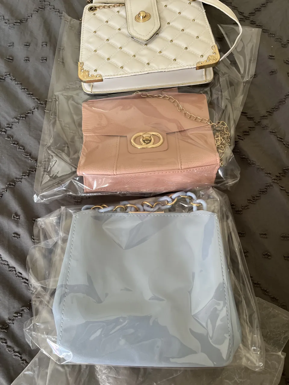 Set de 3 carteras de colores. La cartera blanca es acolchada con detalles dorados y tachas. La cartera rosa es con un diseño elegante y cadena dorada. La cartera celeste es un modelo tipo tote bag con cadena celeste y dorada. Ideales para complementar cualquier look. 20x20 todas