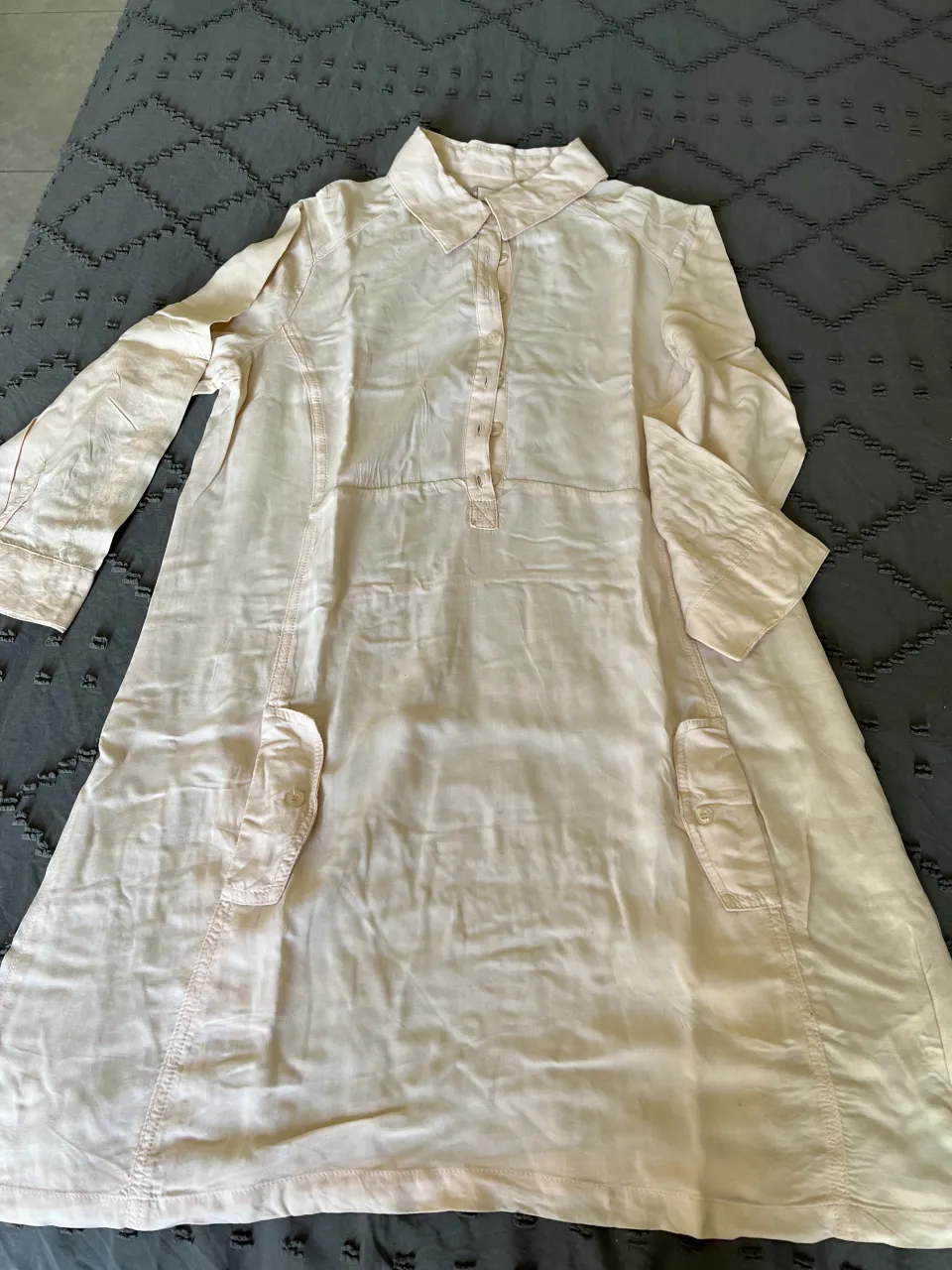 Camisa larga de lino color rosa pálido, con botones al frente y bolsillos con tapa. Ideal para un look casual y fresco. detalle en la costura de la etiqueta