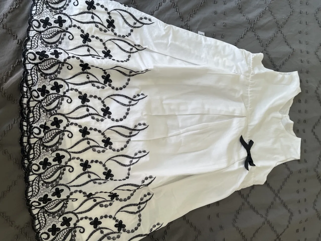 Vestido blanco con bordado negro en la falda y un moño negro en el frente. Ideal para niñas, perfecto para eventos especiales o para el día a día en primavera y verano.