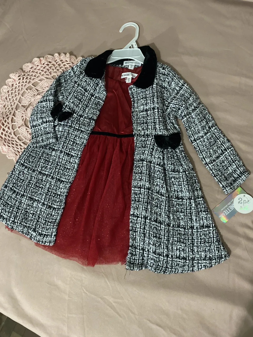 Conjunto de vestido rojo con brillos y saco tweed blanco y negro. El vestido es sin mangas y tiene detalles de tul con glitter. El saco tiene cuello y puños de terciopelo negro y dos moños negros en los bolsillos.