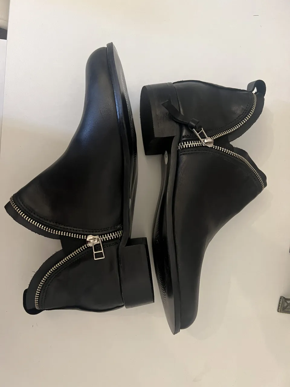 Botitas negras de cuero con cierre metálico plateado a los costados y detalle de tira en la parte trasera.