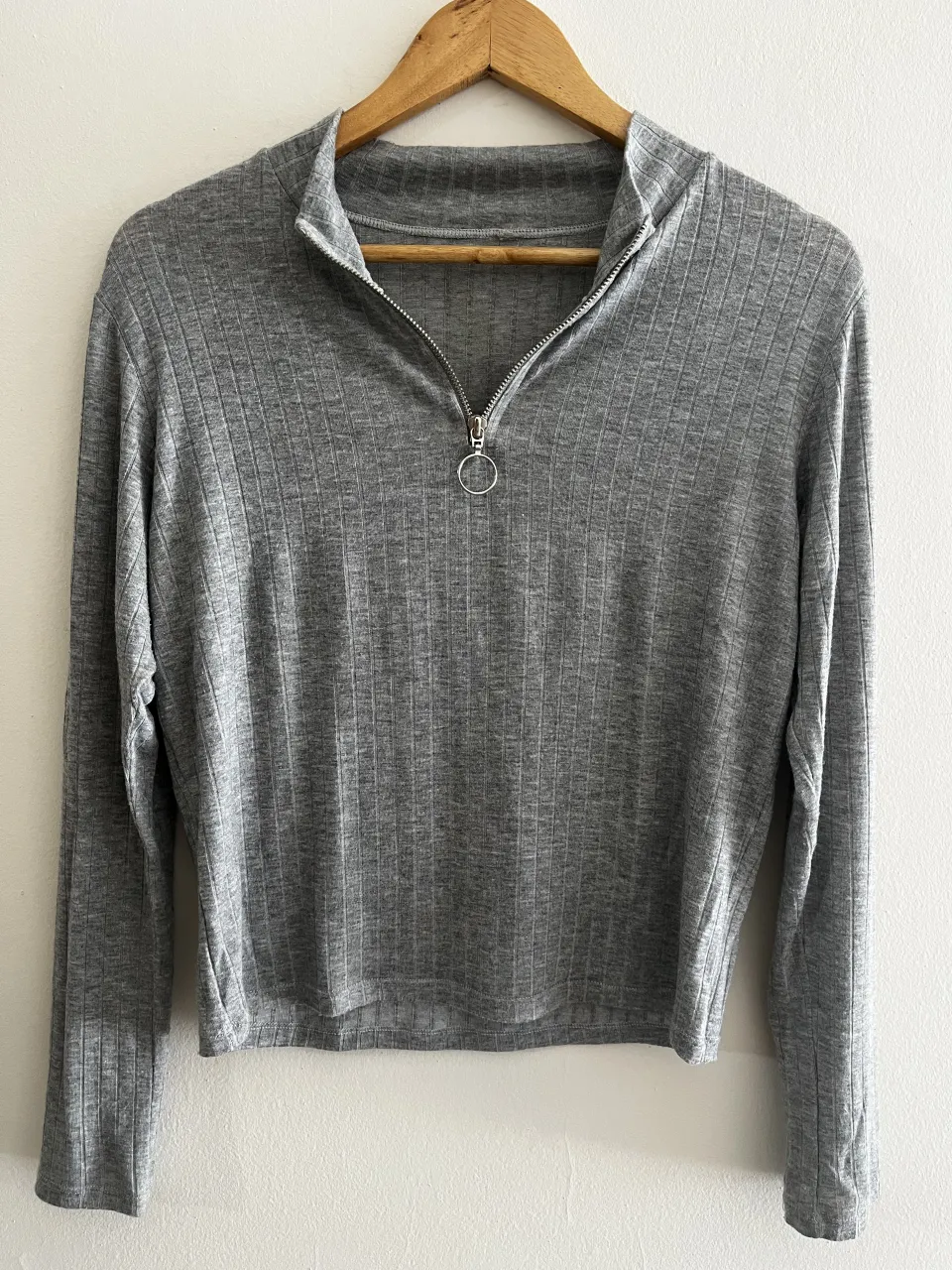 Remera gris de manga larga con cuello alto y cierre metálico con aro al frente.