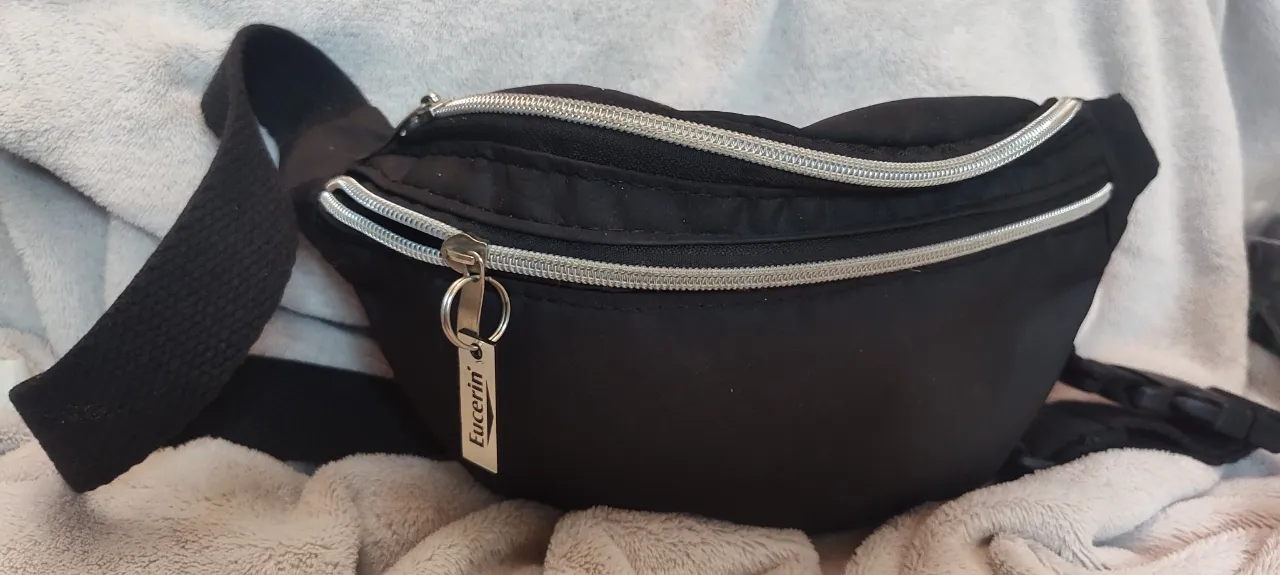 Riñonera negra con dos cierres plateados y un llavero con la marca Eucerin.