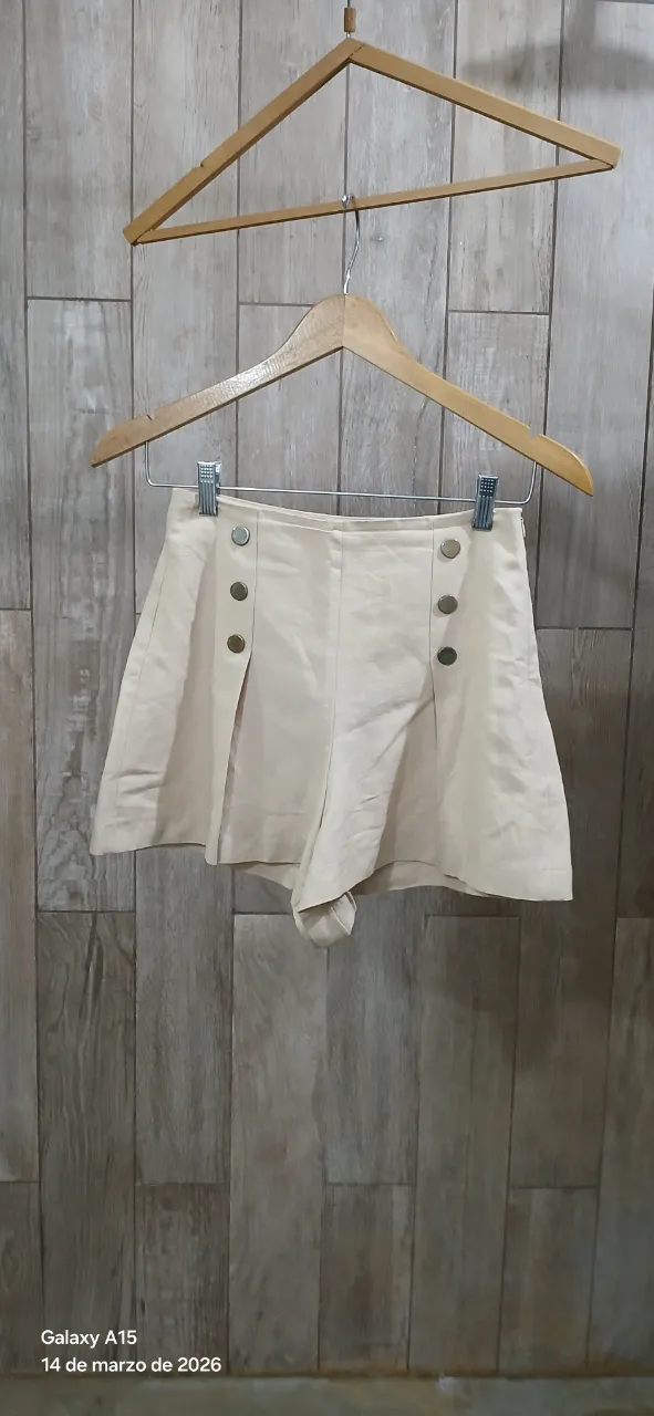 Shorts color beige con cuatro botones dorados en la parte delantera. Cierre invisible lateral. Algodón, lino y viscosa.