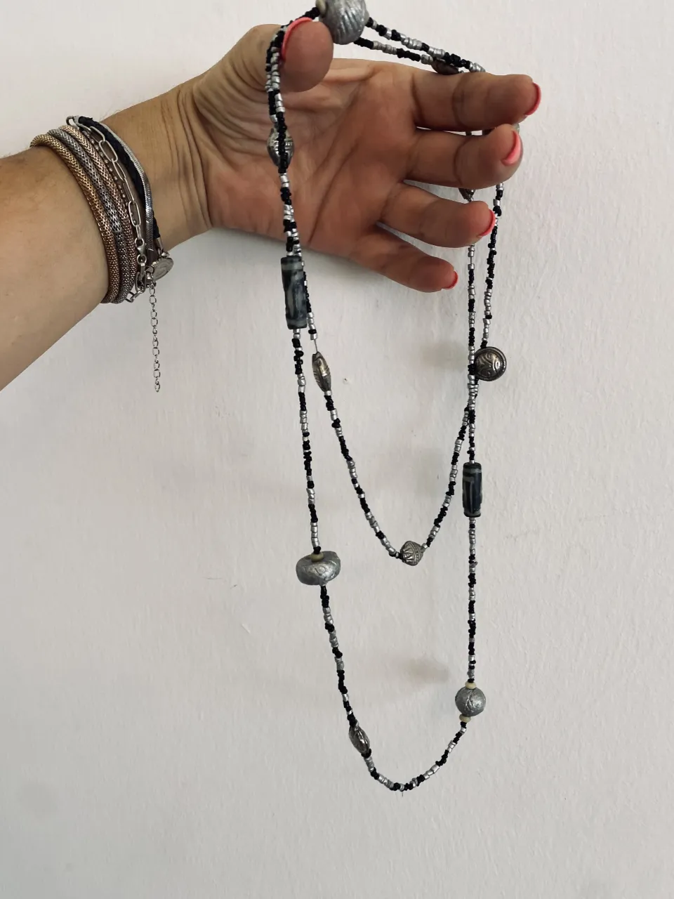 Collar largo con cuentas negras y plateadas. Tiene cuentas cilíndricas y esféricas de metal con detalles grabados.