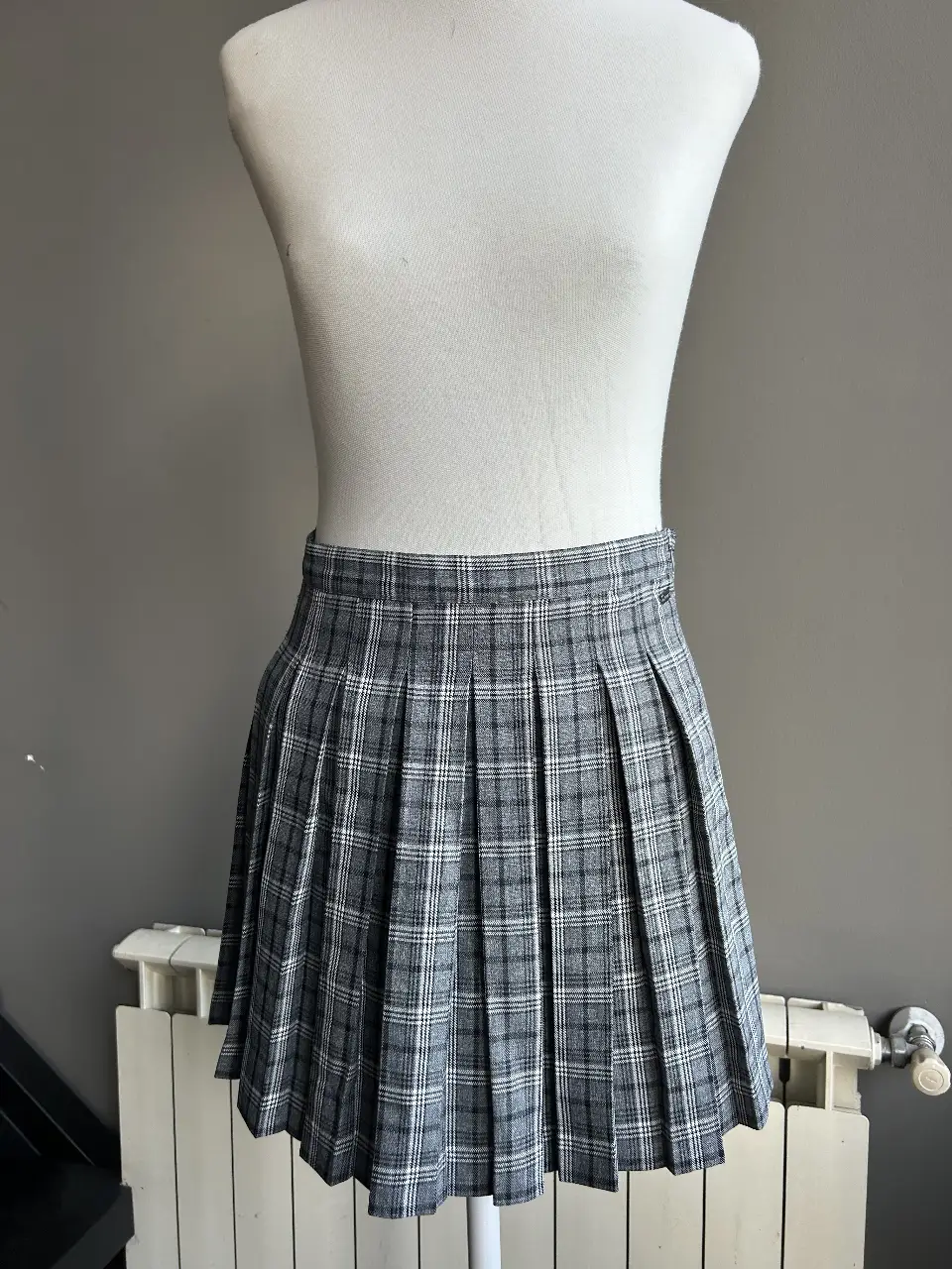 Pollera tableada de corte mini, con estampado a cuadros en tonos grises y blancos. Ideal para un look colegial o casual.