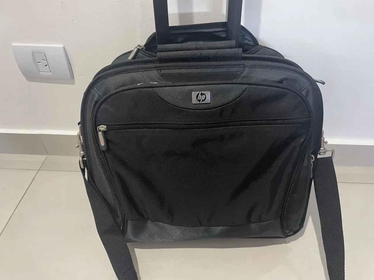 Maletín negro con ruedas y manija extensible. Posee correa de hombro desmontable. Tiene múltiples compartimentos con cierre.